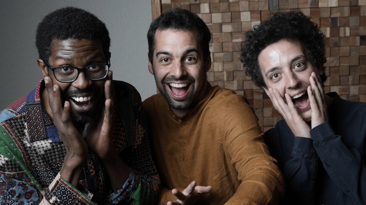 Gruppebilde av bandet, i farger. Alle ser mot kamera og geiper, smilende.