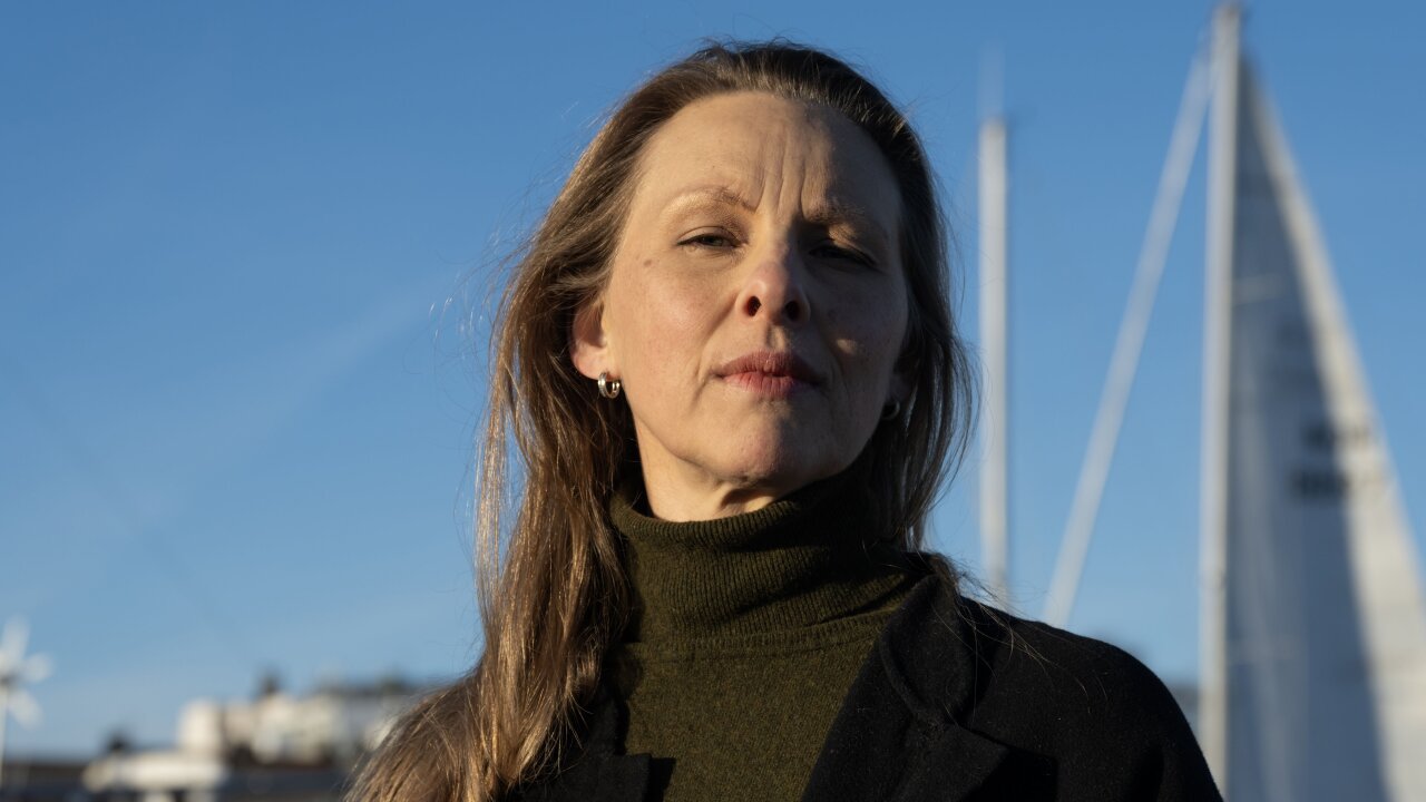 Portrett av Torun Eriken. Hun kikker alvorlig mot kamera. I bakgrunnen, blå himmel hvor man skimter en seilbåt.